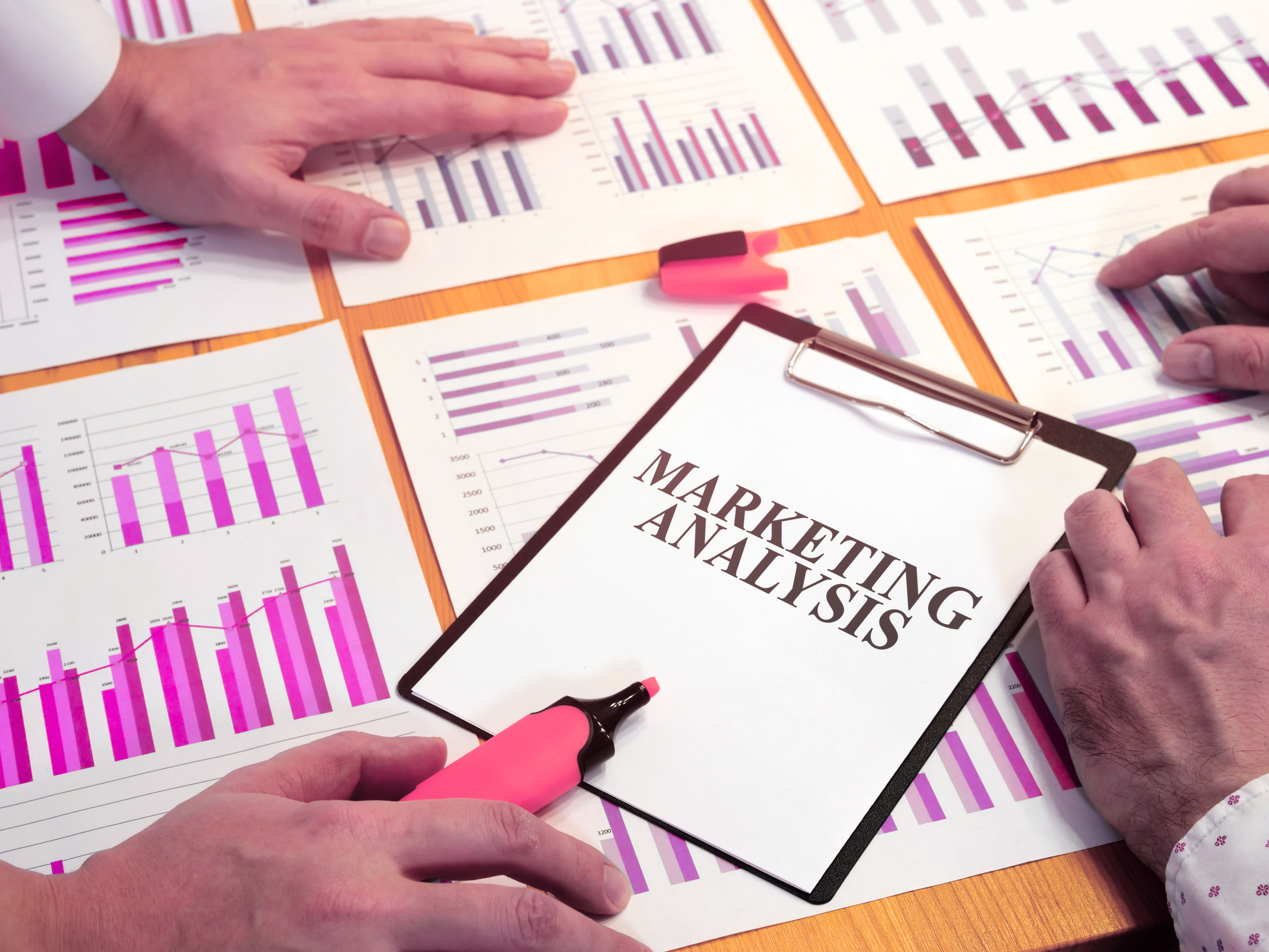 Marketing analysis documents and charts being reviewed by a team, showing performance tracking and revenue-focused planning