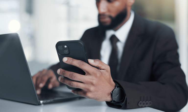 Business professional using a smartphone and laptop to verify secure account access with multi-factor authentication.